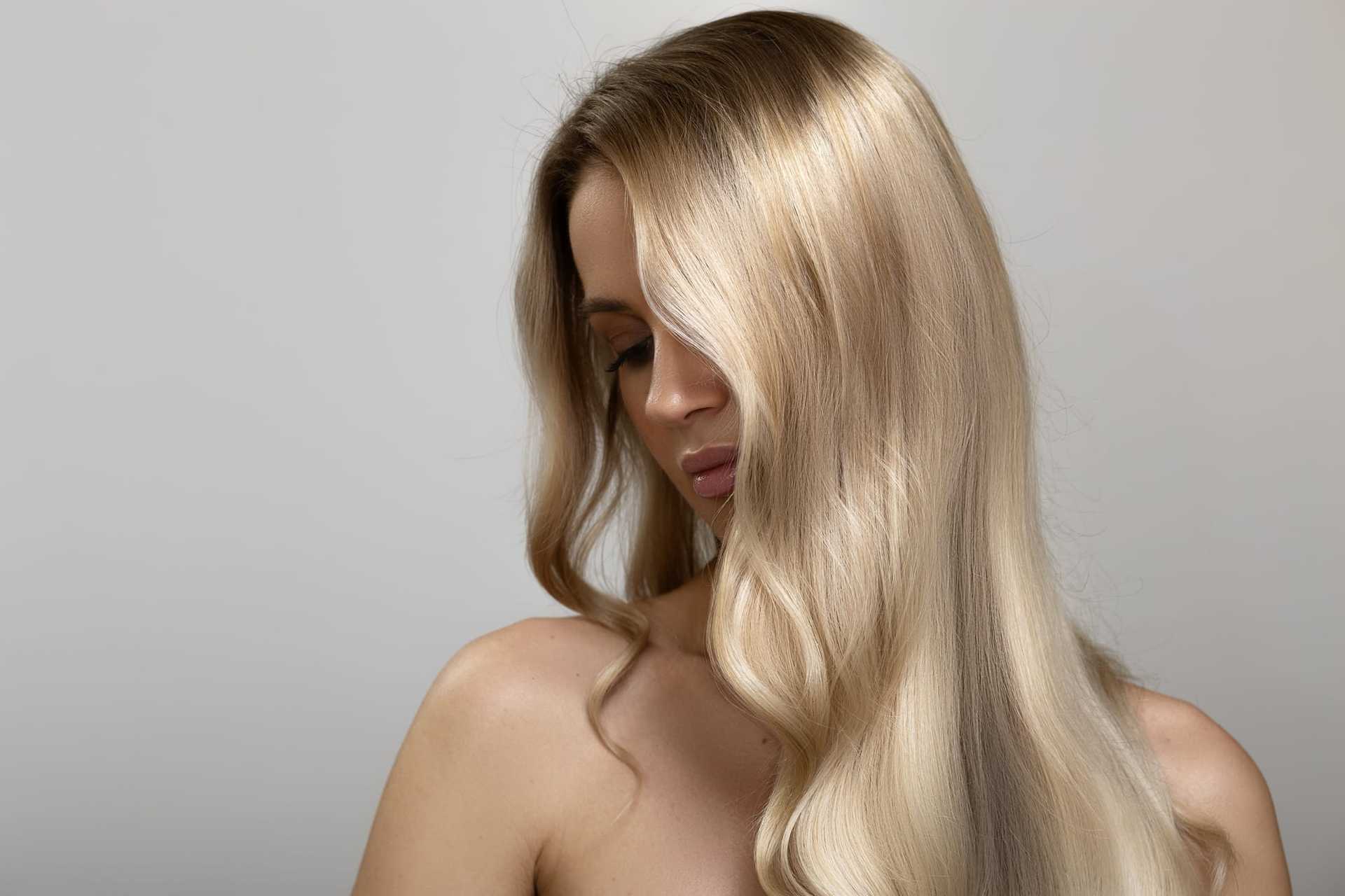 Blonde woman with closed eyes, long wavy hair, and serene expression against a neutral background.