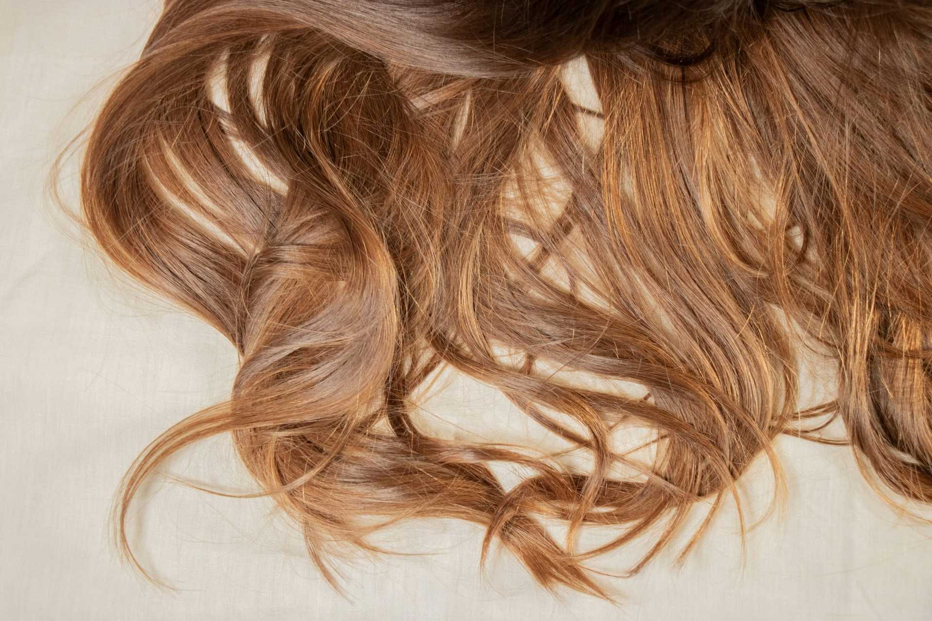 Close-up of wavy, light brown hair spread on a cream surface.