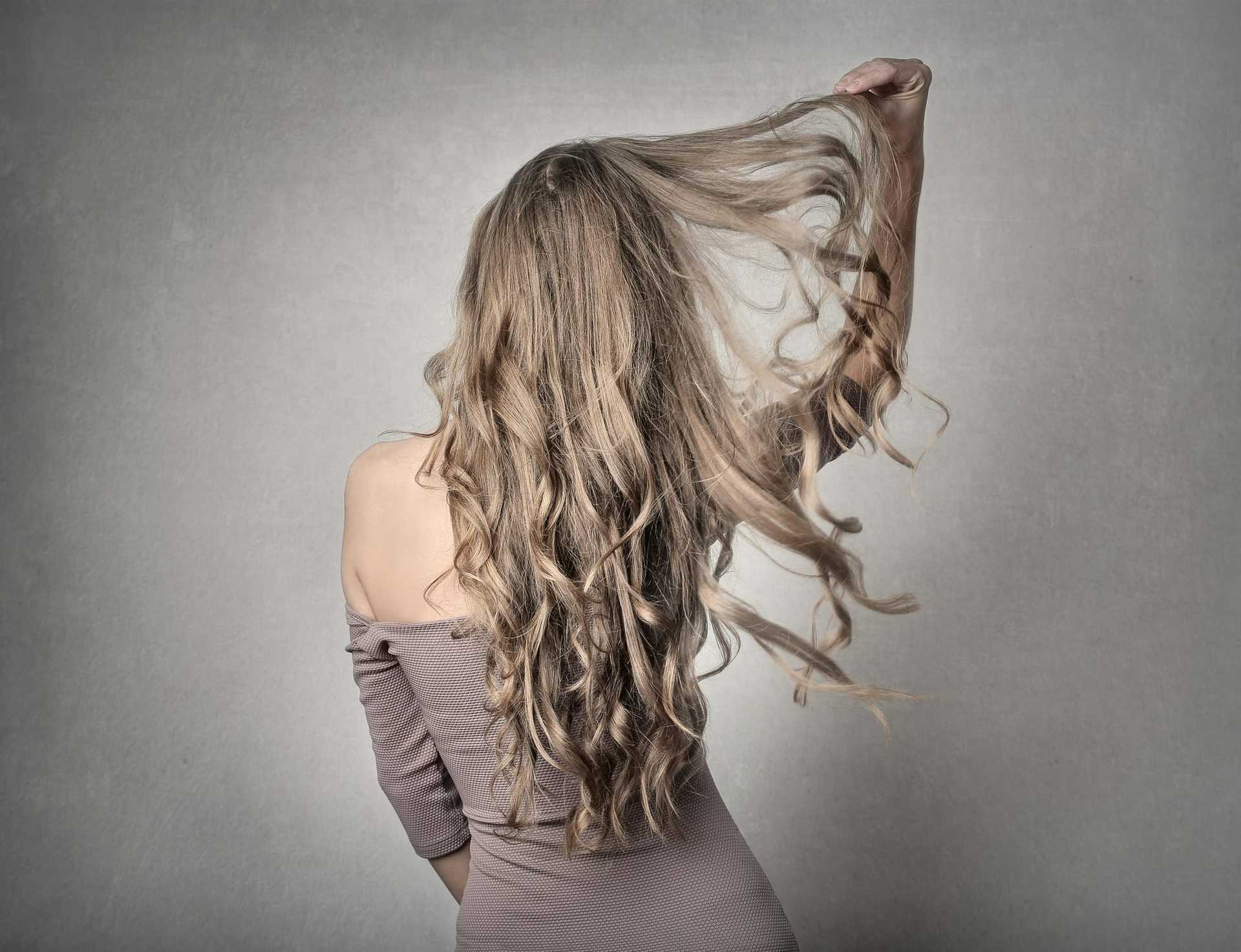 Woman with wavy blonde hair, back turned, in an off-shoulder dress.